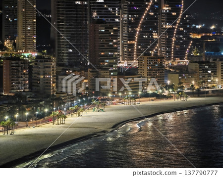 Serene Beach With City Lights At Night, Calm Coastal Scenery Illuminated Under City Skyline At Night Serene Beach With City Lights At Night, Calm Coastal Scenery Illuminated Under City Skyline At Night 137790777