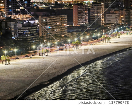 Calm Seaside Stroll, Silent Shoreline Walkway With Gentle Illumination And City Skyline Reflections 137790778