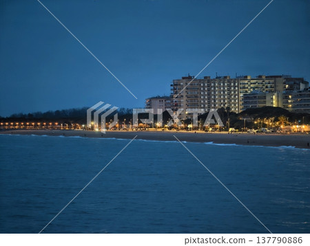 Tranquil Coastal Scene Featuring Luminous Lights Reflecting On Serene Blue Waters Below Darkening Evening Sky Tranquil Coastal Scene Featuring Luminous Lights Reflecting On Serene Blue Waters Below Darkening Evening Sky 137790886