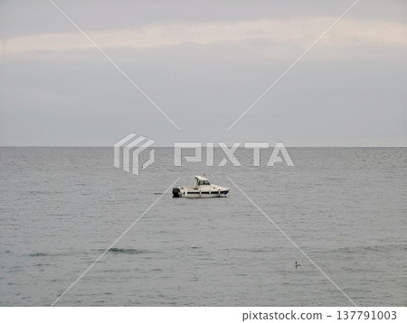 Isolated Vessel On Peaceful Water, Single Motorized Boat Drifting In Calm Grey Ocean Beneath Cloudy Sky Isolated Vessel On Peaceful Water, Single Motorized Boat Drifting In Calm Grey Ocean Beneath Cloudy Sky 137791003