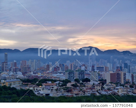 Peaceful Sunset Over City Skyline Featuring Radiant Mountain Ranges And Shimmering Sea Horizon 137791048