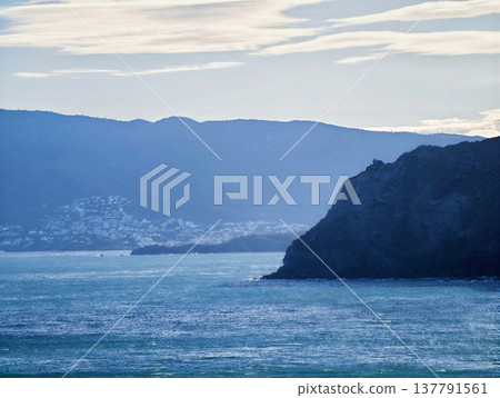Misty Coast With Distant Hills And Calm Waters, Quiet Seashore Silhouette With Soft Glow Over Mountains 137791561