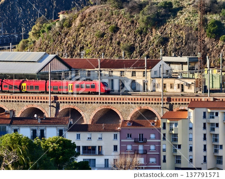 Vibrant Depiction Of Red Train Journeying Through Terraced Cityscape With Stone Bridge And Sunset Glow Vibrant Depiction Of Red Train Journeying Through Terraced Cityscape With Stone Bridge And Sunset Glow 137791571