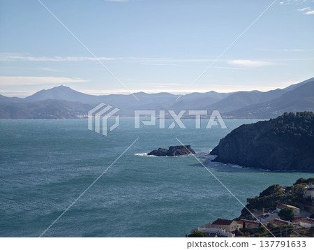 Rocky Promontory With Distant Peaks, Beachfront Village With Mountain Background And Tranquil Sea 137791633