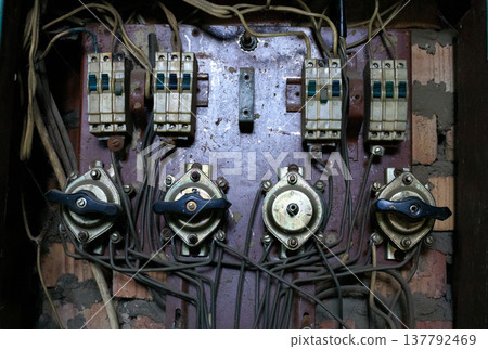 Old electrical panel, vintage switches, and tangled wires. Close-up obsolete industrial fuse box with aged components mounted 137792469