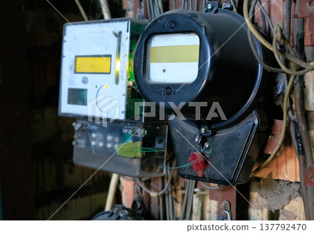 Old analog electricity meter stands alongside a modern digital replacement in a weathered interior Old analog electricity meter stands alongside a modern digital replacement in a weathered interior 137792470