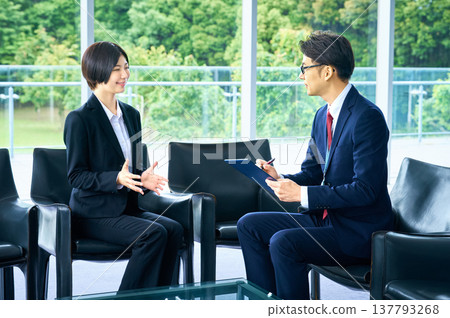 一位女求職者在面試中一邊回答面試官的問題一邊進行自我介紹，而一位男面試官則在一旁做筆記。 137793268