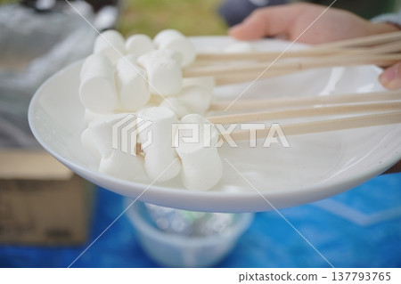 烤棉花糖串在竹籤上擺放在盤子裡，是燒烤甜點的一種食材。 137793765