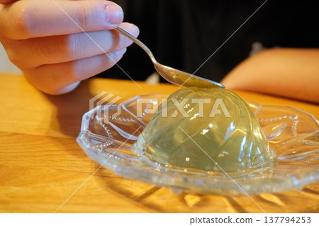 A close-up of hands eating jelly with a spoon. A scene of enjoying homemade dessert at home. A close-up of hands eating jelly with a spoon. A scene of enjoying homemade dessert at home. 137794253