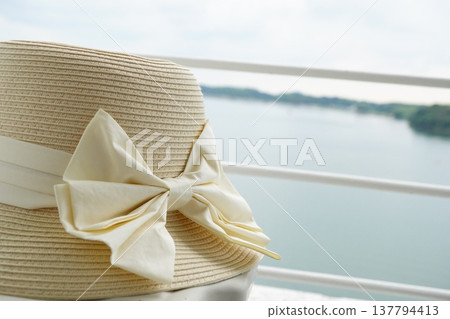 A close-up of a straw hat with a ribbon placed against a lake backdrop. Summer travel, summer resorts, women's summer fashion. 137794413