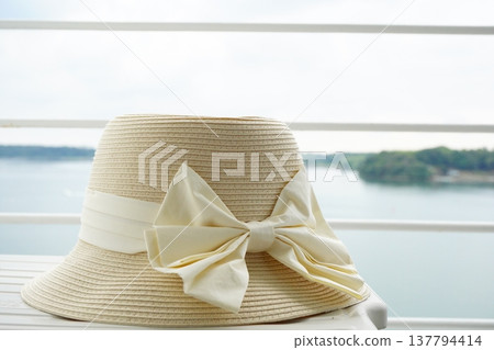 A summery image featuring a straw hat with a ribbon placed on a table. 137794414