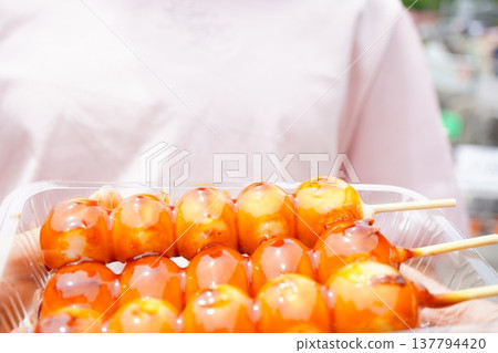 A Japanese confection consisting of skewered rice dumplings with sweet and savory sauce, served in a clear container. A close-up of the dumplings covered in the sweet and savory sauce. 137794420