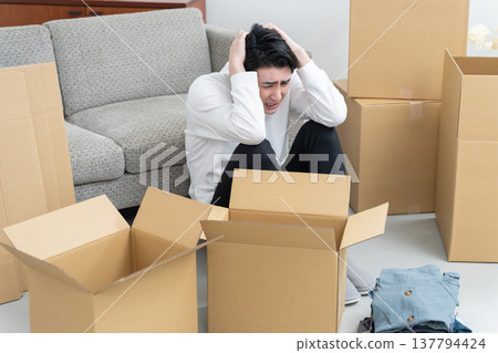 A man who hasn't finished packing for his move (cardboard boxes, tidying up, organizing) A man who hasn't finished packing for his move (cardboard boxes, tidying up, organizing) 137794424