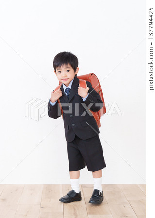 一名小學一年級男生背著書包(參加入學典禮,穿著正式西裝)。 一名小學一年級男生背著書包(參加入學典禮,穿著正式西裝)。 137794425