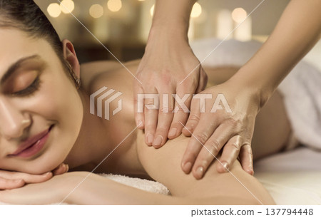 Relaxed woman receiving shoulder massage in spa with warm candlelight ambience Relaxed woman receiving shoulder massage in spa with warm candlelight ambience 137794448
