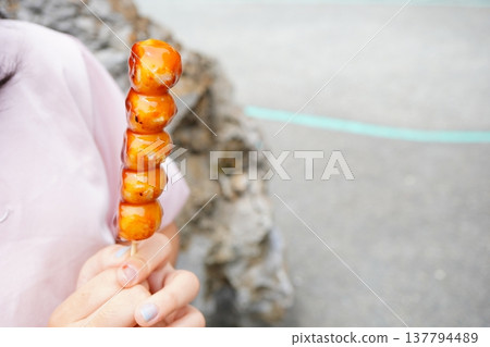 特寫鏡頭拍攝的是一個孩子手持御手洗團子。這種傳統的日式點心閃閃發光，裹滿了甜鹹適口的醬汁。 137794489
