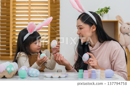 mother and preschool child girl wearing bunny ears holding colorful egg while celebrating together at home on easter day. happy family holiday activity concept mother and preschool child girl wearing bunny ears holding colorful egg while celebrating together at home on easter day. happy family holiday activity concept 137794758