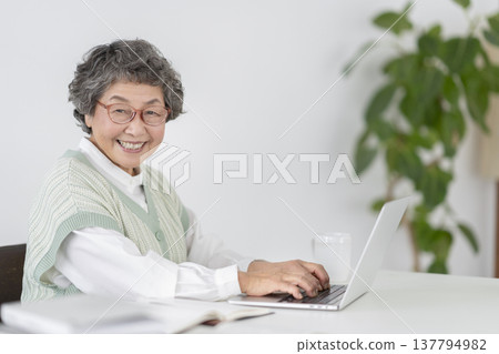 An 80-year-old woman working on her laptop, smiling and looking directly at the camera in a portrait. An 80-year-old woman working on her laptop, smiling and looking directly at the camera in a portrait. 137794982