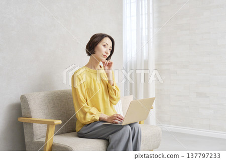 A woman using a computer in the living room thinking A woman using a computer in the living room thinking 137797233