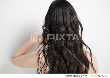 A woman with long, permed hair flowing in the wind against a white background; her face is obscured, and she is shown from behind. A woman with long, permed hair flowing in the wind against a white background; her face is obscured, and she is shown from behind. 137797857