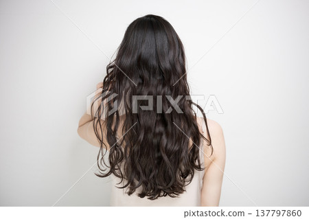 A woman with long, permed hair flowing in the wind against a white background; her face is obscured, and she is shown from behind. A woman with long, permed hair flowing in the wind against a white background; her face is obscured, and she is shown from behind. 137797860