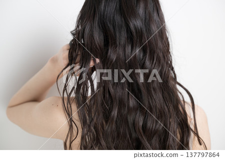 A woman with long, permed hair flowing in the wind against a white background; her face is obscured, and she is shown from behind. A woman with long, permed hair flowing in the wind against a white background; her face is obscured, and she is shown from behind. 137797864
