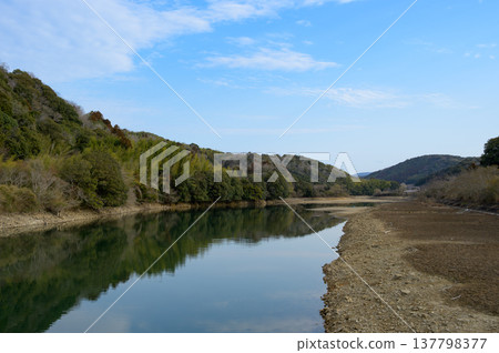 A tranquil lakeside landscape with exposed shorelines stretching out under a blue sky. 137798377