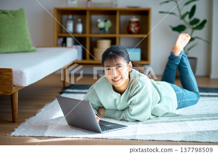 休息日,一位面帶微笑的女士躺在家裡的客廳裡,享受電腦帶來的樂趣。 休息日,一位面帶微笑的女士躺在家裡的客廳裡,享受電腦帶來的樂趣。 137798509