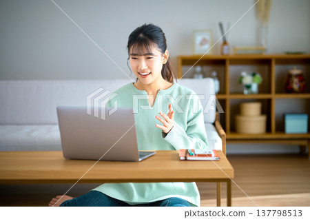 A smiling woman at home, watching an online meeting on her laptop. 137798513