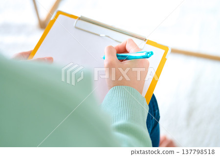 A woman's hands writing on a clipboard; an image of a medical questionnaire, survey, or counseling session. 137798518