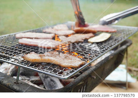 A close-up of outdoor cooking: meat, sausages, and vegetables grilled over charcoal on a barbecue grill. 137798570
