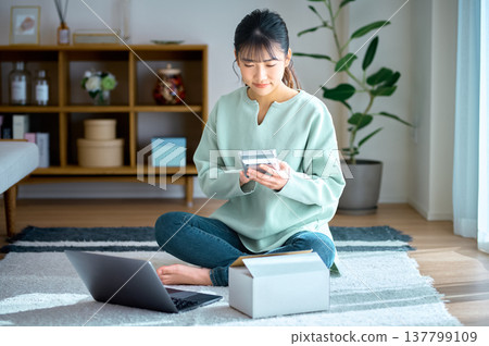 A woman who has successfully managed her household finances is smiling as she taps away on her calculator. A woman who has successfully managed her household finances is smiling as she taps away on her calculator. 137799109
