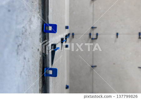 Close-up of blue and black plastic leveling spacers installed between large format tiles on an interior corner. 137799826