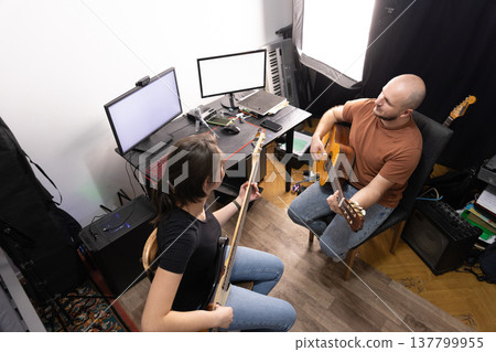 High angle shot of a male guitarist and female bassist rehearsing in a home music studio environment. 137799955