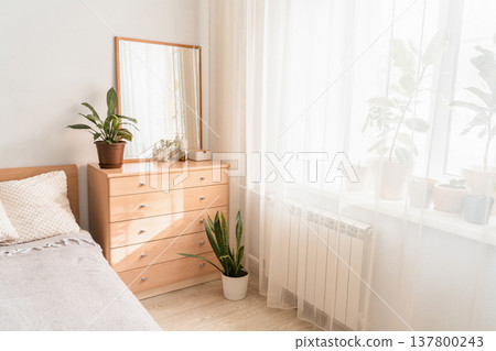 Wooden dresser in a modern bedroom interior, displaying a mirror, decorative plant, and various beauty bottles on top 137800243