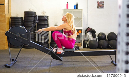 Woman exercising on rowing machine in well equipped gym Woman exercising on rowing machine in well equipped gym 137800943