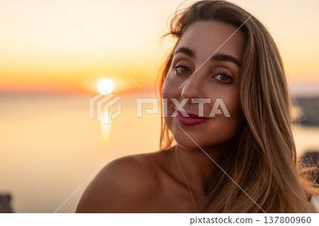 Woman portrait sunset beautiful young woman smiling at the camera during a golden hour sunset over the calm sea Woman portrait sunset beautiful young woman smiling at the camera during a golden hour sunset over the calm sea 137800960
