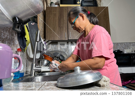 Senior woman washing dishes and metal pot lid in kitchen sink, elderly lady doing domestic chores at home, household routine portrait Senior woman washing dishes and metal pot lid in kitchen sink, elderly lady doing domestic chores at home, household routine portrait 137801108