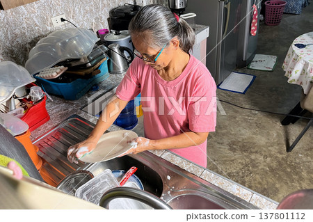 Senior woman scrubbing plate with soapy sponge in kitchen sink, elderly lady focused on washing dishes, domestic household routine Senior woman scrubbing plate with soapy sponge in kitchen sink, elderly lady focused on washing dishes, domestic household routine 137801112