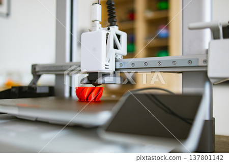 A modern 3D printer is actively creating a vibrant red object layer by layer on its build plate A modern 3D printer is actively creating a vibrant red object layer by layer on its build plate 137801142