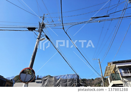Utility pole with a dense network of electrical transmission and communication lines under a clear blue sky in Japan. Utility pole with a dense network of electrical transmission and communication lines under a clear blue sky in Japan. 137801288