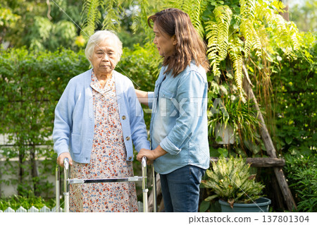 Doctor caregiver help and care Asian senior woman patient walk with walker in park at hospital. 137801304