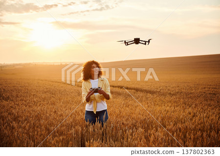 With drone that is flying. Beautiful woman is on the wheat agricultural field With drone that is flying. Beautiful woman is on the wheat agricultural field 137802363