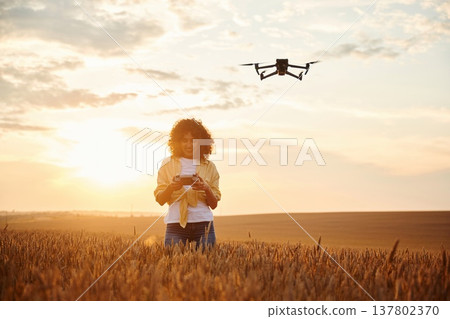 Modern black drone is up. Beautiful woman is on the wheat agricultural field 137802370