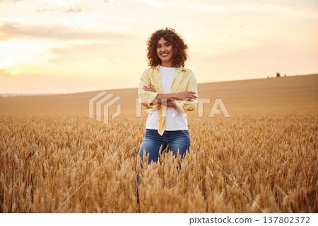 Standing with arms crossed. Beautiful woman is on the wheat agricultural field Standing with arms crossed. Beautiful woman is on the wheat agricultural field 137802372