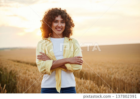 Standing with arms crossed. Beautiful woman is on the wheat agricultural field Standing with arms crossed. Beautiful woman is on the wheat agricultural field 137802391