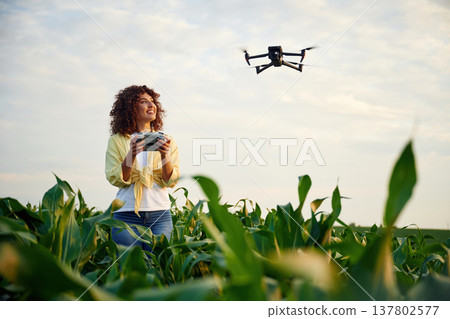 Little help from a drone, controlling it. Woman is on the corn agricultural field Little help from a drone, controlling it. Woman is on the corn agricultural field 137802577