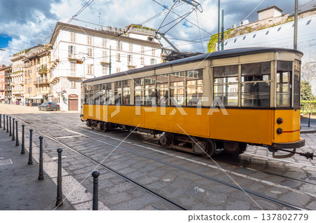 Milan, italy, april 1, 2024. Iconic yellow tram passing through milan historic brera district on cloudy day, vintage streetcar on cobblestone tracks amid classic facades Milan, italy, april 1, 2024. Iconic yellow tram passing through milan historic brera district on cloudy day, vintage streetcar on cobblestone tracks amid classic facades 137802779