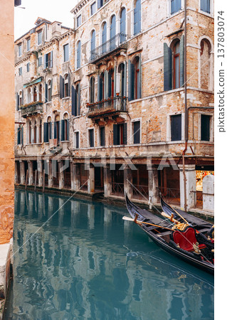 Venice gondola glides through canal next to old buildings under cloudy sky 137803074