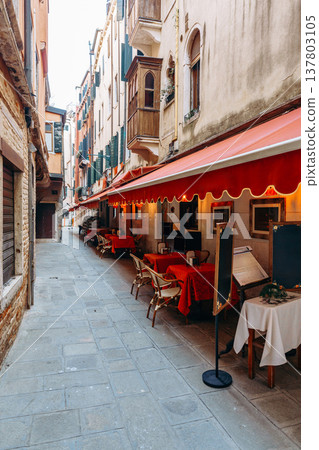 Quiet street in Venice with empty tables and chairs under red awnings in the evening Quiet street in Venice with empty tables and chairs under red awnings in the evening 137803105